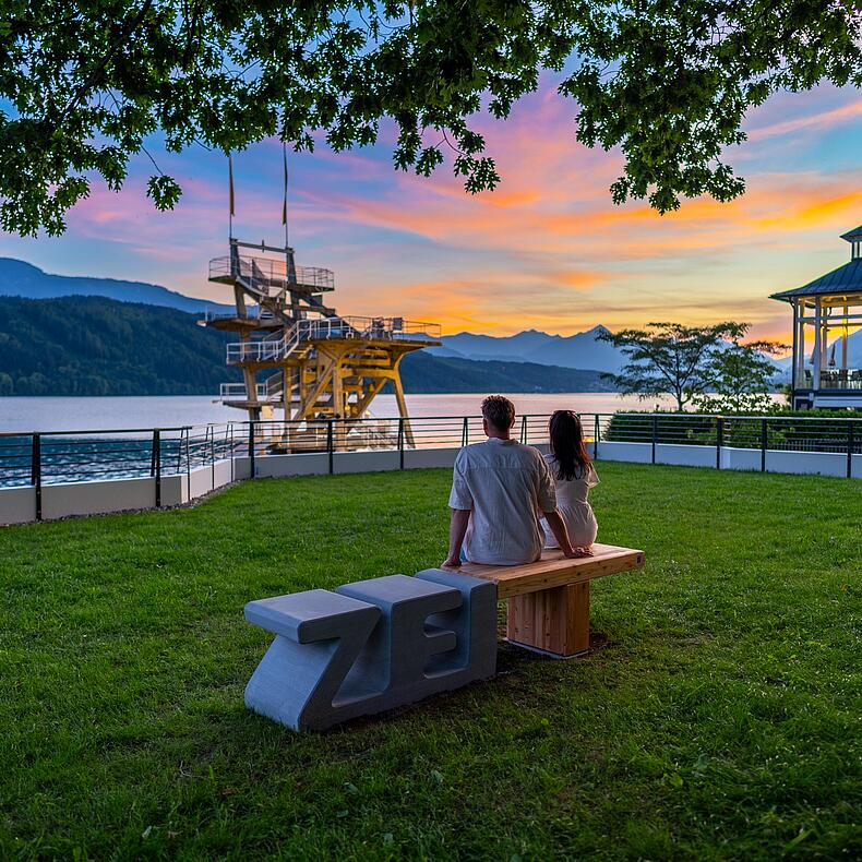 Pärchen sitzt am Abend auf Zeitbank und sieht sich den Sonnenuntergang an