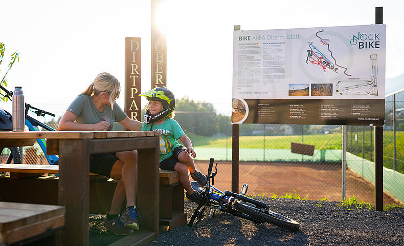 Mutter macht mit Kind Pause vom mountainbiken an einem Tisch in der Bike Area Obermillstatt