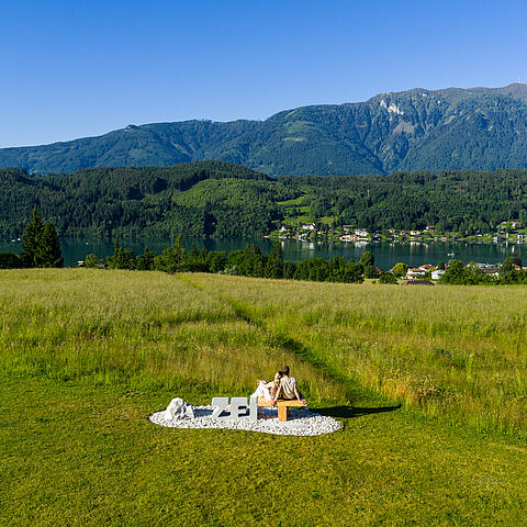 Pärchen sitzt auf Zeitbank und genießt das Berg- und Seepanorama