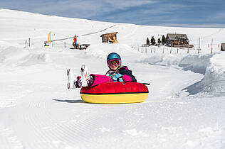 Kind fährt mit einem Tubing-Reifen den Berg hinunter
