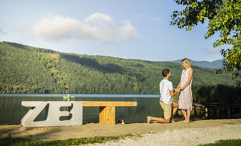 Pärchen steht vor der ZEITbank und Mann kniet vor Frau und macht ihr einen Heiratsantrag 