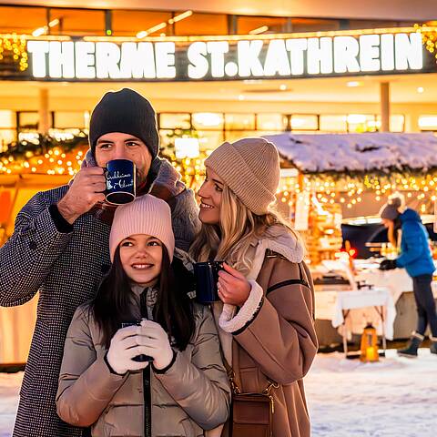 Glückliche Familie steht am Kirchheimer Adventmarkt und trinkt ein ein heißes Getränk
