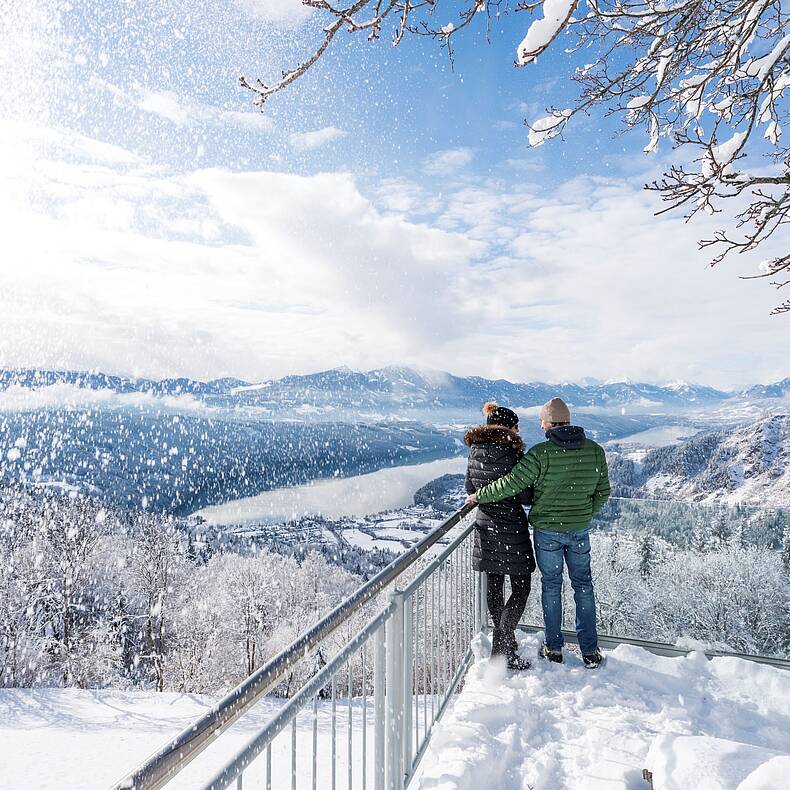 Pärchen steht im Winter am Sternenbalkon und schaut auf den Millstätter See