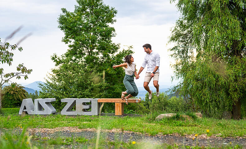 Pärchen springt zusammen von der Zeitbank beim Natur Gut Lassen