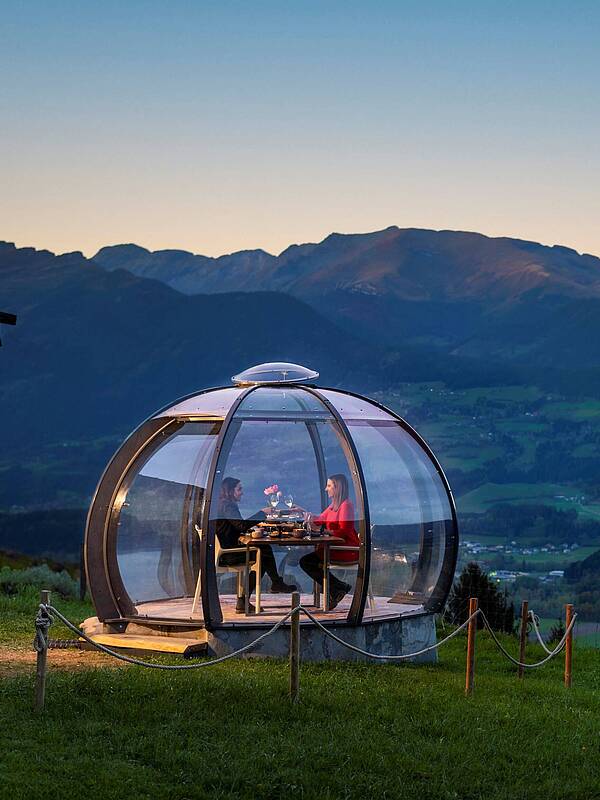 2 Personen genießen ihr Dinner in der Glaskuppel in einer Sommernacht