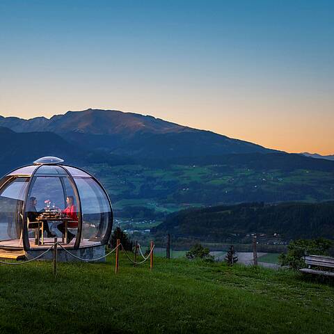 2 Personen genießen ihr Dinner in der Glaskuppel in einer Sommernacht