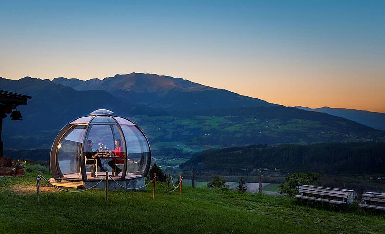 2 Personen genießen ihr Dinner in der Glaskuppel in einer Sommernacht