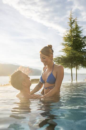 Mann hebt Frau im Außenpool des Badehauses mit Ausblick auf den Millstätter See hoch