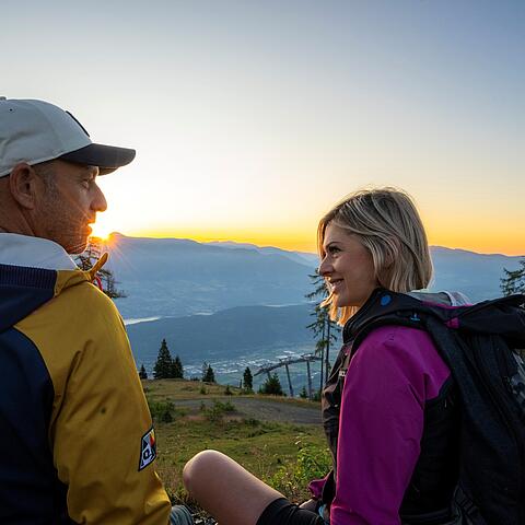 Pärchen sitzt auf der Zeitbank und genießt den Sonnenaufgang am Goldeck